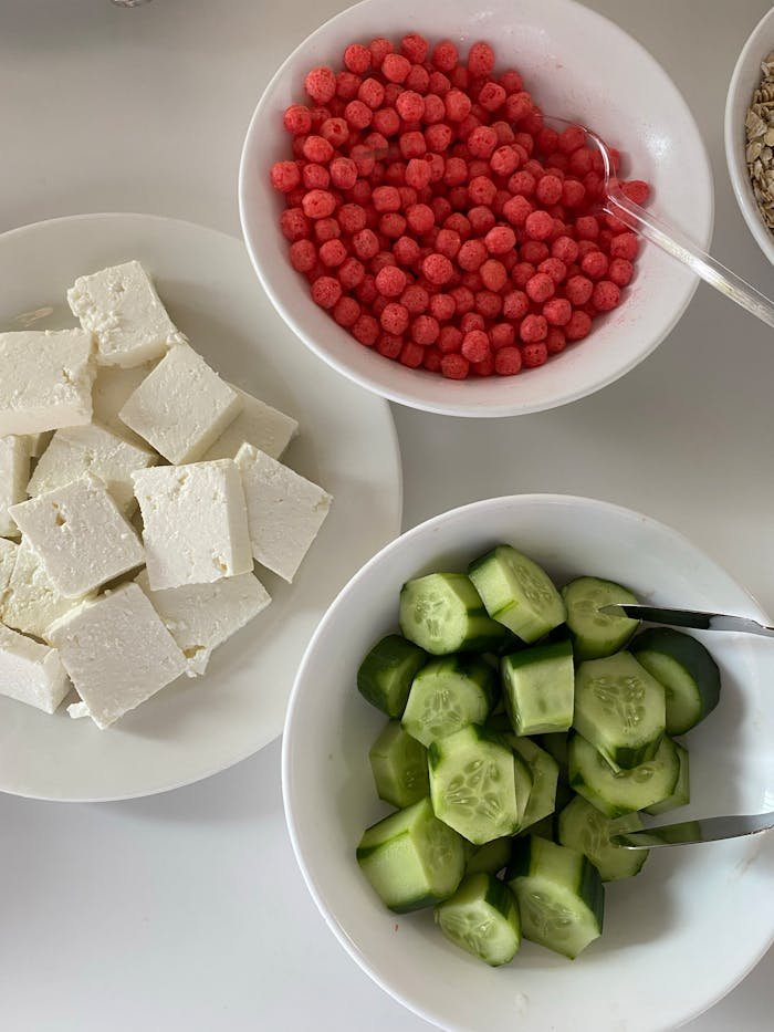 Top view of feta cubes, cucumbers, and red berries in bowls for healthy eating.
