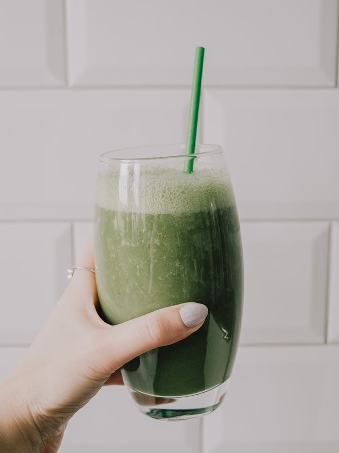 A hand holding a vibrant green smoothie with a straw, showcasing a healthy lifestyle.
