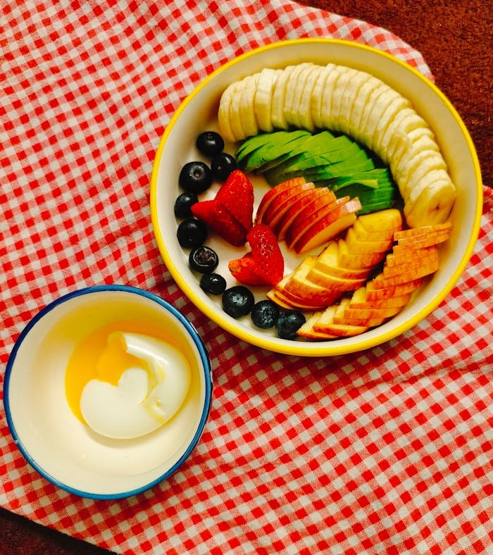 Top view of a vibrant fruit platter with yogurt on a red checkered tablecloth.