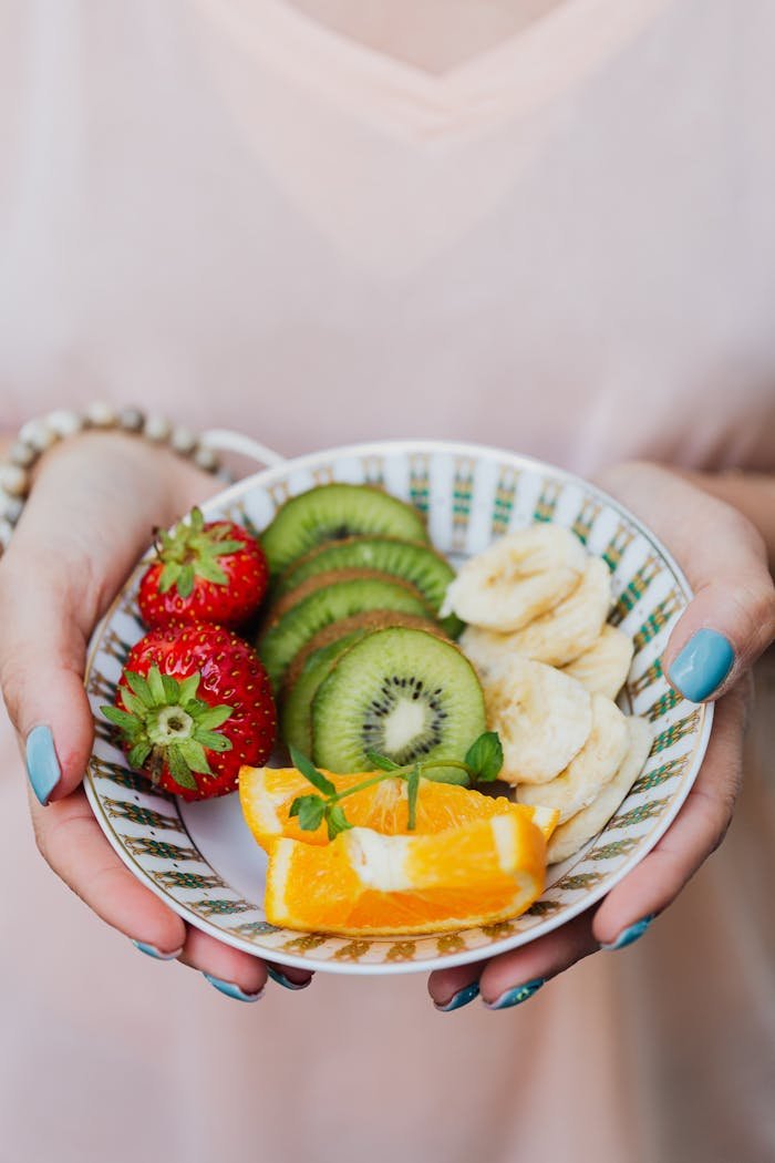 Vibrant fruit bowl with strawberries, kiwi, banana, and orange slices held in hands.