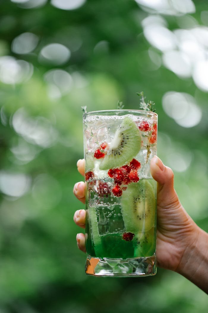 Hand holding a refreshing kiwi and berry infused drink in a tall glass outdoors.